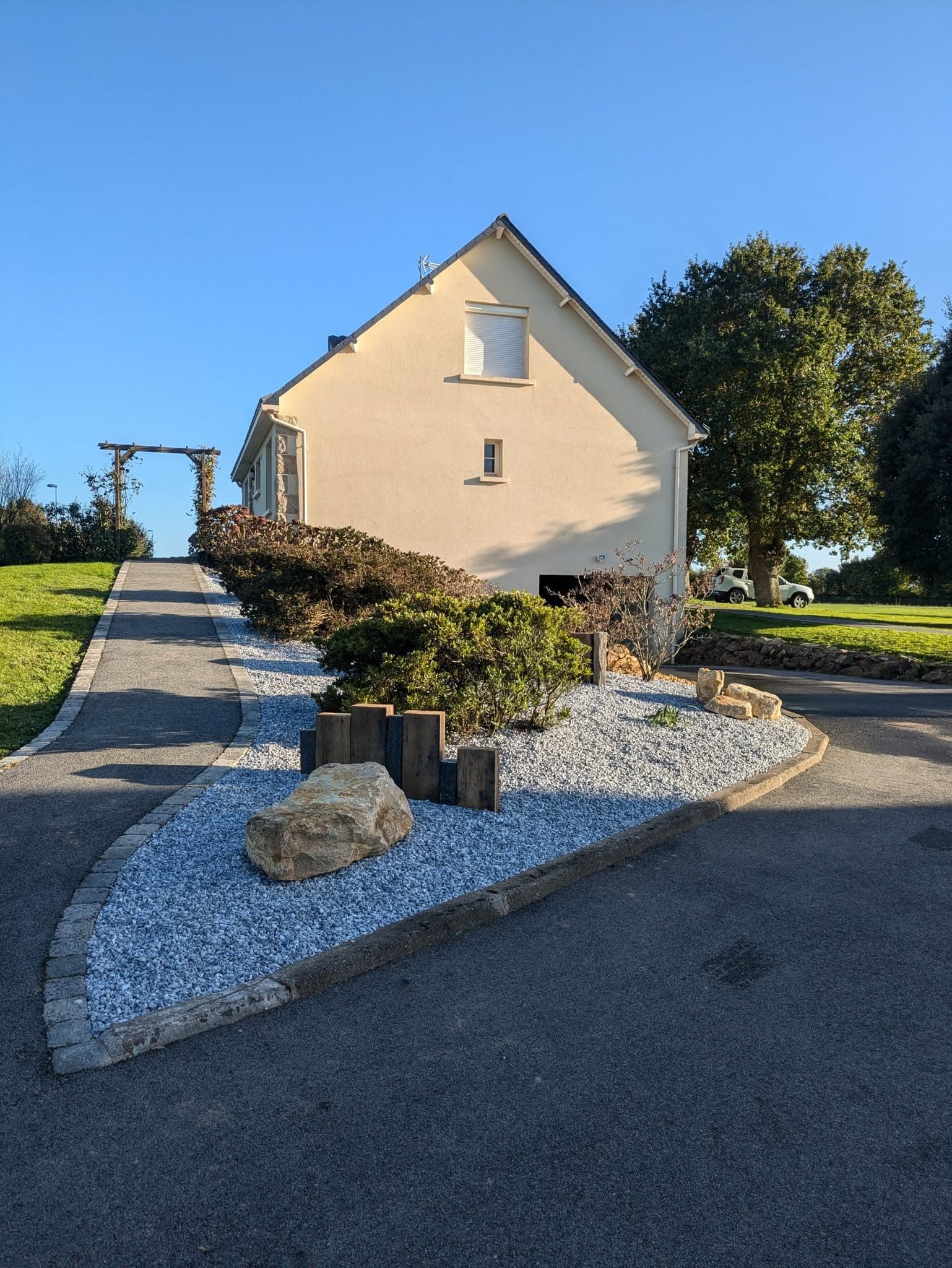 Aménagement paysager minéral réalisé par Dauffy Paysage : massif de gravier, roche et traverses bois devant une maison