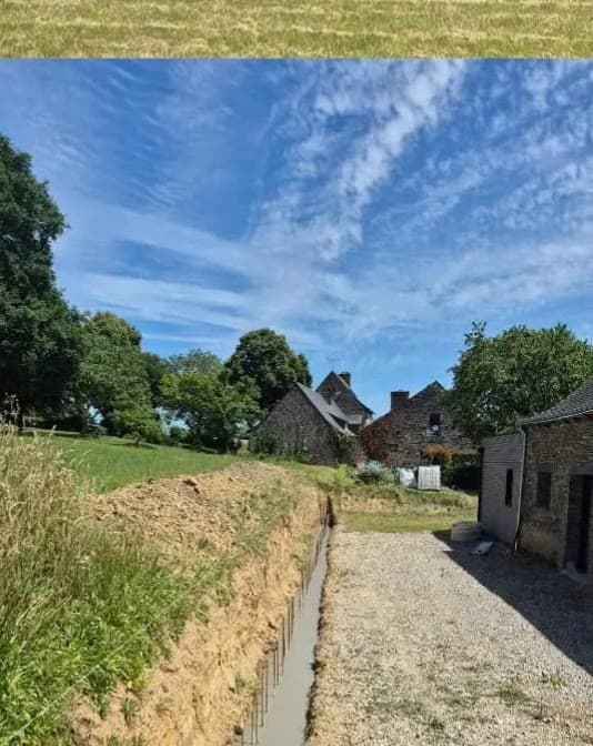 Tranchée bétonnée le long d'un accès gravillonné, longères en pierre